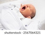 Cute newborn baby boy yawning on white bed. The baby is 7 days old.