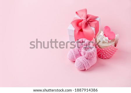 Cute newborn baby girl shoes with festive decoration cupcake and gift box  over pink background. Baby shower, birthday, invitation or greeting card idea, copy space, flyer, invitation, monochrome