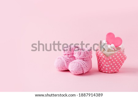Cute newborn baby girl shoes with festive decoration cupcake over pink background. Baby shower, birthday, invitation or greeting card idea, copy space, flyer, invitation, monochrome concept