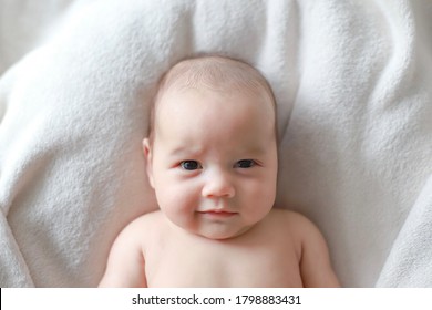 Cute newborn baby head shot  portrait making funny face. Mixed race Asian-German infant healthy smiling top view. Kid lying on white blanket he is about 8 weeks or 2 month old.
