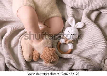 Cute newborn baby in knitted booties with toy bunny lying on light grey plaid, top view