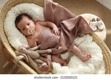 Cute newborn baby with pacifier and toy bunny lying in cradle at home, top view
