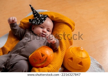 Cute newborn boy lifestyle portrait. Infant child lying on knitted blanket with carved pumpkins.
