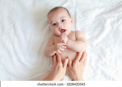 Cute newborn boy open mouth making funny face during his mother massaging belly after bathing. Happy mixed race Asian-German infant oil massage relaxing time top view.