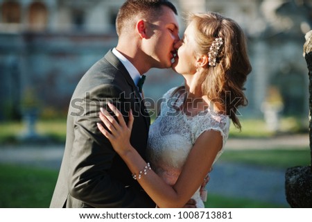 Cute newly married couple kissing next to an old fountain on their wedding day.