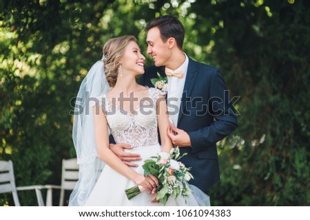 Cute newlyweds hugging and smiling in a green park. Portrait of the bride and groom in a lace dress.