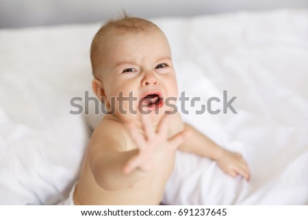Cute nice little baby girl crying lying with her mom on bed at home.