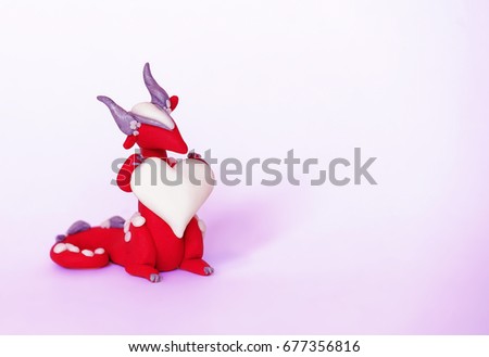 Cute nice little romantic toy dragon with white heart for congratulations on a pink purple background with a soft focus.