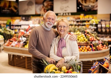 A cute old couple in love is hugging at the supermarket and purchasing while smiling at the camera. - Powered by Shutterstock