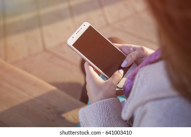 Cute Ordinary Caucasian Brunette Woman In Casual Outfit Working On A Phone While Walking At The Nature Park. Cold Spring (autumn) Weather, Warm Coat On A Girl. Sunset. Copy Space