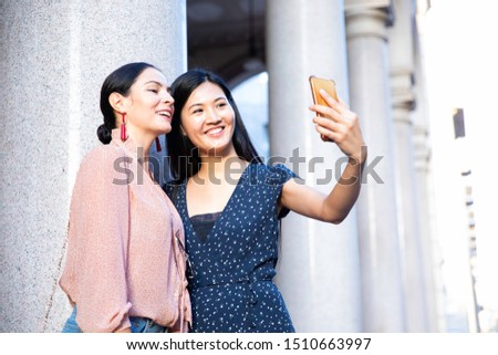 Cute outdoor portrait of funny pretty best friends asian girls having fun making selfie at city center, positive crazy emotions, traveling together in milan, italy, Europe