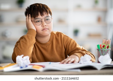 Cute overweight japanese boy teenager doing school project at home, sitting at desk with books and notebooks, got tired and bored, looking for creative solutions, closeup photo, copy space