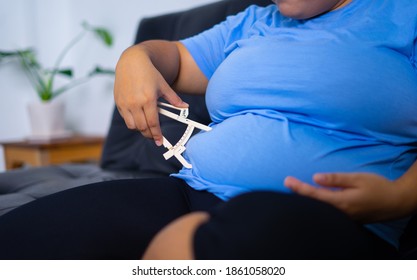 Cute Overweight Woman Using Skin Fold Caliper Measure The Thickness Of A Fold Her Skin On Her Belly To Estimate The Total Percent Of Body Fat On Her Body.