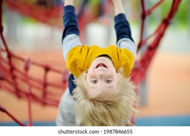 Cute perky Preschooler Junge mit Spaß auf dem Spielplatz im Freien. Sommerliche oder Sommerferien oder Herbst aktive Sportmöglichkeiten für Kinder. Outdoor Aktivitäten für Familien mit Kindern.