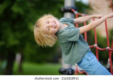 Cute perky preschooler boy having fun on outdoor playground. Spring or summer or autumn active sport leisure for child. Outdoor activities for family with children. Equipment of entertainment park - Shutterstock ID 2161818911