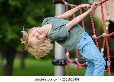 Cute perky preschooler boy having fun on outdoor playground. Spring or summer or autumn active sport leisure for child. Outdoor activities for family with children. Equipment of entertainment park - Shutterstock ID 2161825409