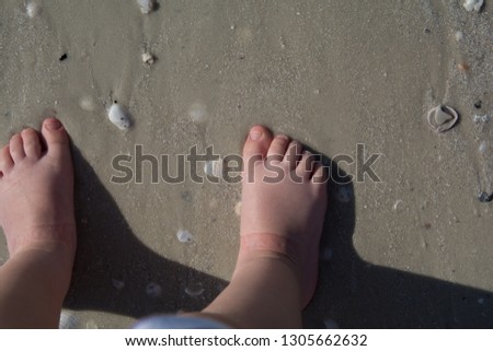 Cute photo of a child's feet in in sand on a sandy beach with seashells while on a summer holiday, barefoot toddler walking on the sand