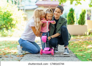 Cute photo of LGBT family spending time in the park. Happy foster girl riding her scooter and receiving kisses and hugs from loving mothers. - Powered by Shutterstock