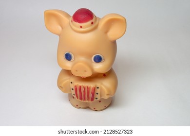 cute piglet with big blue eyes toy, in little hat and colored polka dots jumpsuit playing at concertina, closeup