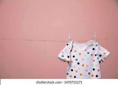 Cute Polka Dot Baby Body Suit Hanging From A Line Against A Pink Background