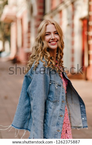Cute positive girl with curly hair turns and looks into the camera with a smile in a beautiful denim jacket