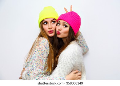 Cute Positive Portrait Of Best Friend Pretty Young Girls, Winter Time, Neon Hats, Cozy Sweaters, Hugs And Having Fun, Natural Glowing Makeup, Two Sisters Sending Air Kiss, Joy, Couple, Emotions.