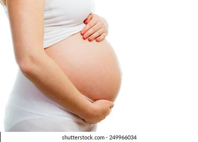 Cute pregnant belly isolated on white. Side view of young pregnant woman embracing her naked abdomen with hands. Big belly on the third trimester of pregnancy close-up. Concept of pregnant life.
