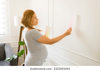 Cute pregnant woman holding color swatches and trying to choose the best color for painting the baby nursery room - Powered by Shutterstock