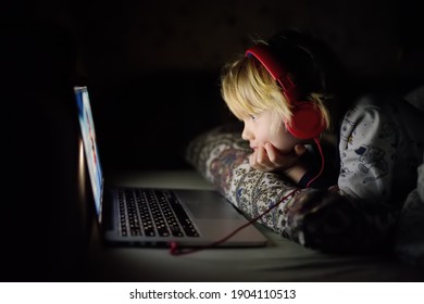 Cute Preschool Boy Wearing Headphones Is Watching Cartoon Movie By Laptop Before Sleeping In Bed Or Early In The Morning Right After Waking Up. Overuse And Addiction Kids From Gadgets. 