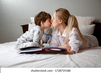 Cute Preschool Child Son Holding A Book Reading Fairy Tales For Mom, Lying In Bed Together, Happy Mother Listening Focused Little Baby Boy Learning To Read Relaxing In The Bedroom Enjoy Bedtime Storie