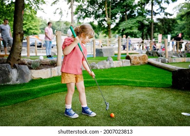 Cute Preschool Girl Playing Mini Golf With Family. Happy Toddler Child Having Fun With Outdoor Activity. Summer Sport For Children And Adults, Outdoors. Family Vacations Or Resort.