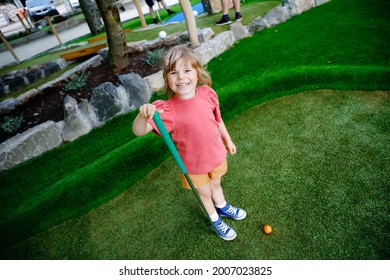 Cute Preschool Girl Playing Mini Golf With Family. Happy Toddler Child Having Fun With Outdoor Activity. Summer Sport For Children And Adults, Outdoors. Family Vacations Or Resort.