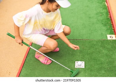 Cute Preschool Girl Playing Mini Golf With Family. Happy Child Having Fun With Outdoor Activity. Summer Sport For Children And Adults, Outdoors. Family Vacations Or Resort.