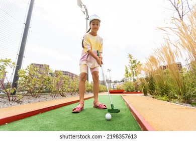 Cute Preschool Girl Playing Mini Golf With Family. Happy Child Having Fun With Outdoor Activity. Summer Sport For Children And Adults, Outdoors. Family Vacations Or Resort.