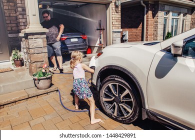 Cute Preschool Little Caucasian Girl Helping Father Wash Car On Driveway In Front House On Summer Day. Child Wiping Cleaning Machine Bumper. Kids Home Errands Duty Chores Responsibility Concept. 