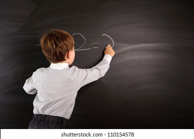Cute preschooler against dark blackboard in classroom