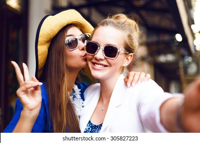 Cute pretty girls making funny selfie on the street, kissing to the cheek, having fun together,  joy, positive, love, friendship, sisters.