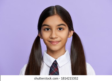Cute pretty smiling indian hispanic tween kid girl with ponytails wearing school uniform standing isolated on lilac violet background. Latin schoolgirl looking at camera, headshot close up portrait.