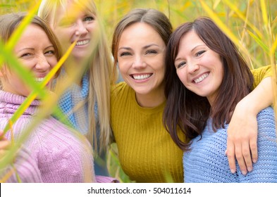 Cute pretty young woman grinning at the camera as she stands arm in arm with three female friends amongst long reeds outdoors - Shutterstock ID 504011614