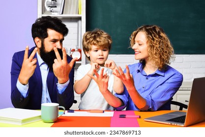 Cute pupil learning math and counting on fingers with parents. Little kid doing math homework with teachers. Boy from elementary school with parents in classroom. Mathematics lesson at primary school. - Powered by Shutterstock - Get 15% off with code: PIKWIZARD15