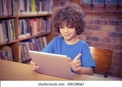 Cute pupil using tablet in the library in school