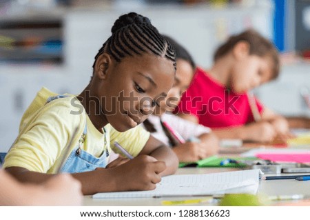 Cute pupil writing at desk in classroom at the elementary school. Student girl doing test in primary school. Children writing notes in classroom. African schoolgirl writing during the lesson.