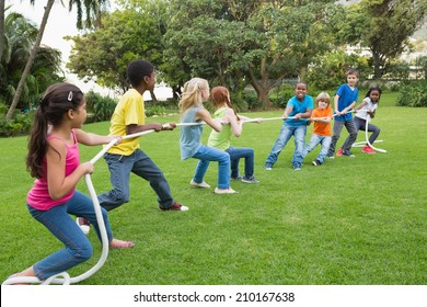 Cute Pupils Playing Tug Of War On The Grass Outside At The Elementary School