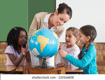 Cute pupils and teacher in classroom with globe at the elementary school - Powered by Shutterstock