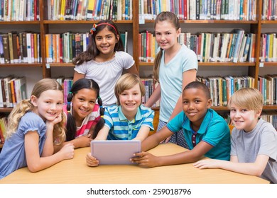 Cute pupils using tablet computer in library at the elementary school
