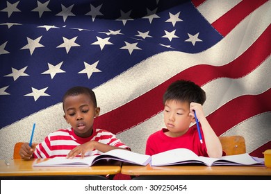 Cute Pupils Writing At Desk In Classroom Against Digitally Generated American National Flag