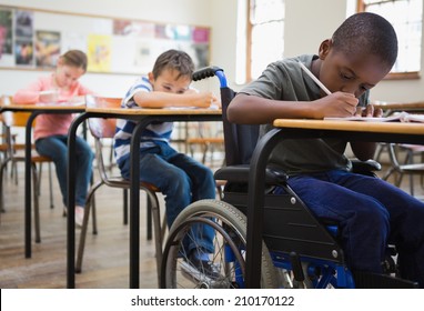 Cute pupils writing at desks in classroom at the elementary school - Powered by Shutterstock