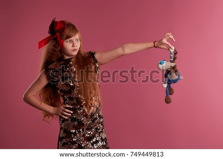 Cute red haired teen girl in gold dress and black shoes with a little hat and toy friend