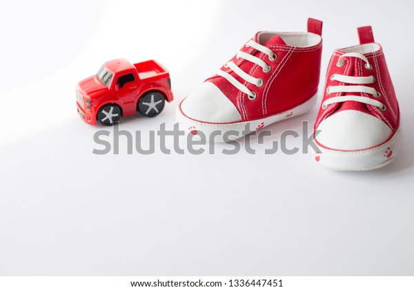Cute red small sized canvas\
shoes with toy car top view on white background with\
copyspace