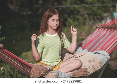 cute red-haired teenage girl sitting on a hammock in the lotus position, yoga outdoors, in the garden, country life, outdoors activities - Powered by Shutterstock